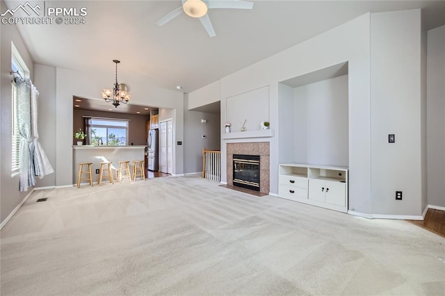 unfurnished living room with a tile fireplace, light carpet, ceiling fan with notable chandelier, and a wealth of natural light