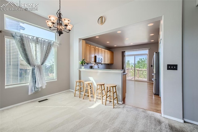 kitchen featuring kitchen peninsula, stainless steel appliances, light colored carpet, pendant lighting, and a notable chandelier