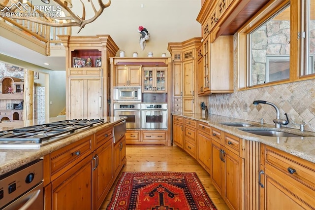 kitchen featuring sink, tasteful backsplash, light stone counters, appliances with stainless steel finishes, and light wood-type flooring