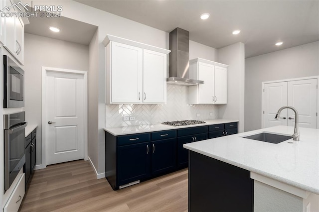 kitchen featuring white cabinets, wall chimney range hood, sink, blue cabinets, and light hardwood / wood-style floors