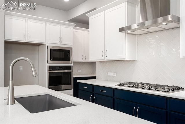 kitchen with blue cabinets, sink, wall chimney exhaust hood, appliances with stainless steel finishes, and white cabinetry