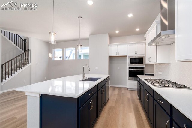 kitchen with pendant lighting, a center island with sink, sink, wall chimney exhaust hood, and appliances with stainless steel finishes