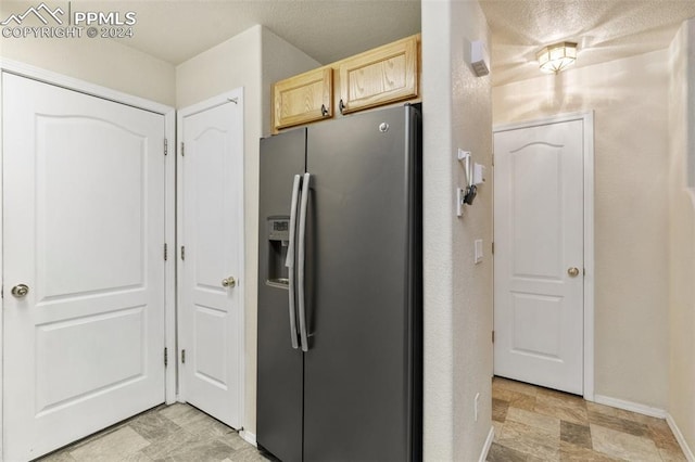 kitchen with stainless steel fridge with ice dispenser, light brown cabinetry, and a textured ceiling