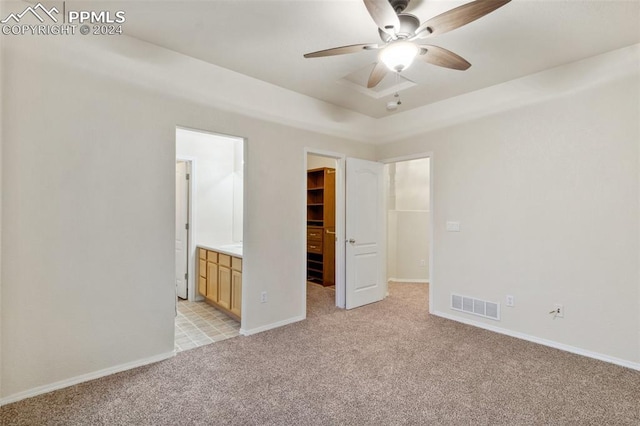 unfurnished bedroom featuring connected bathroom, ceiling fan, a walk in closet, light carpet, and a closet