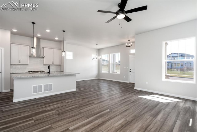 unfurnished living room featuring ceiling fan with notable chandelier and dark wood-type flooring