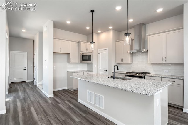 kitchen with a center island with sink, wall chimney exhaust hood, built in microwave, decorative light fixtures, and white cabinetry