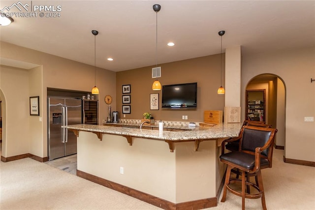 kitchen with high end refrigerator, a kitchen breakfast bar, decorative light fixtures, light colored carpet, and kitchen peninsula