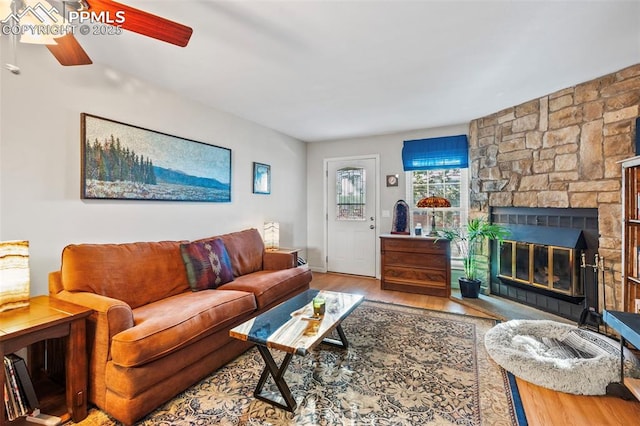 living room featuring hardwood / wood-style floors, ceiling fan, and a stone fireplace