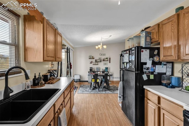 kitchen with a textured ceiling, sink, pendant lighting, an inviting chandelier, and light hardwood / wood-style floors