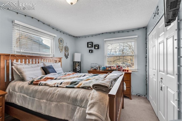 bedroom featuring a wall mounted air conditioner, light carpet, a textured ceiling, and a closet