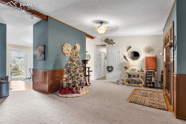 interior space featuring a textured ceiling, light colored carpet, ceiling fan, vaulted ceiling with beams, and wood walls