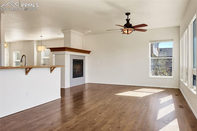 unfurnished living room with ceiling fan with notable chandelier, sink, dark wood-type flooring, and a tiled fireplace