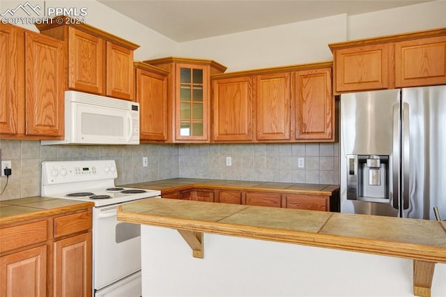 kitchen featuring decorative backsplash, white appliances, tile countertops, and a breakfast bar