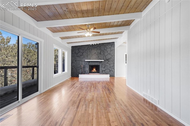 unfurnished living room with wood ceiling, hardwood / wood-style flooring, ceiling fan, beam ceiling, and a stone fireplace