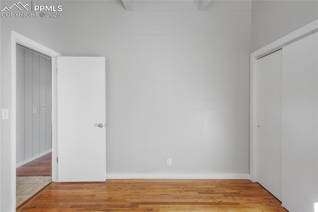 unfurnished bedroom featuring hardwood / wood-style flooring, a closet, and beamed ceiling