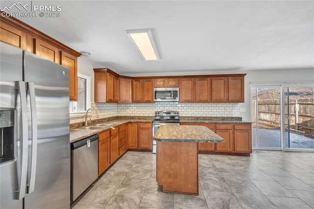 kitchen featuring stainless steel appliances, decorative backsplash, a kitchen island, stone countertops, and sink