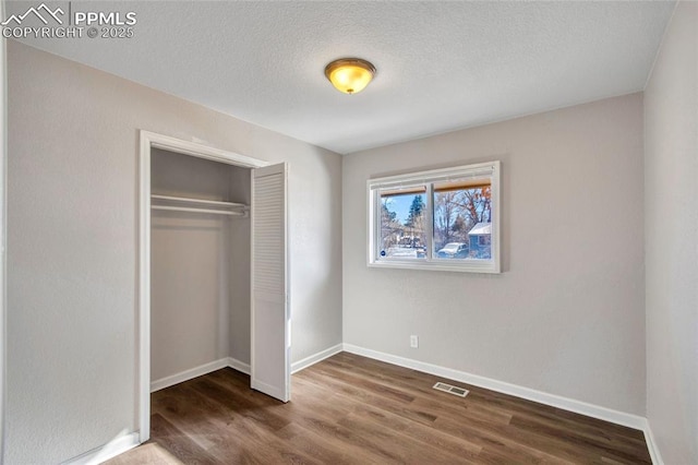 unfurnished bedroom with dark wood-type flooring, a textured ceiling, and a closet