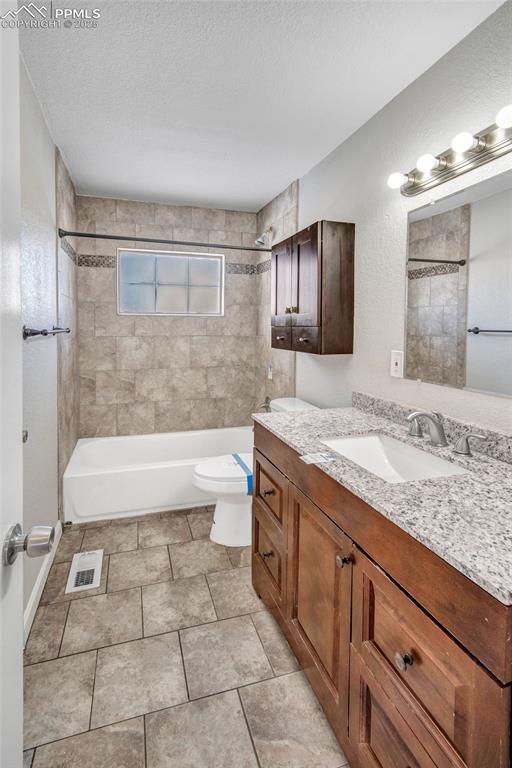 full bathroom with toilet, vanity, a textured ceiling, and tiled shower / bath