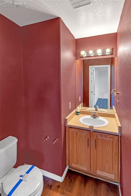 bathroom with hardwood / wood-style flooring, vanity, toilet, and a textured ceiling