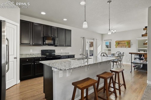 kitchen with sink, pendant lighting, a kitchen bar, a kitchen island with sink, and black appliances