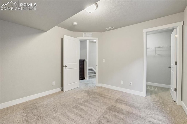 unfurnished bedroom featuring light carpet, a textured ceiling, a spacious closet, and a closet