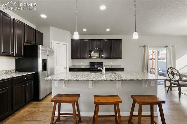 kitchen featuring pendant lighting, black appliances, a center island with sink, and sink