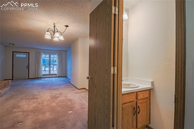 hall with light carpet, a textured ceiling, an inviting chandelier, and sink