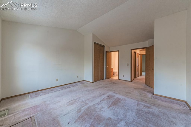 unfurnished bedroom with ensuite bathroom, light colored carpet, lofted ceiling, and a textured ceiling