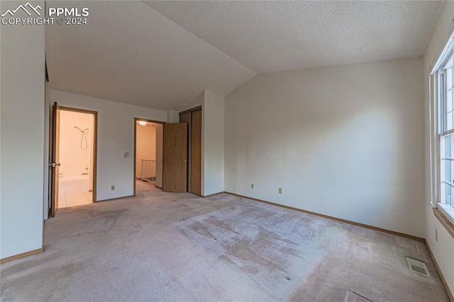 unfurnished bedroom with light carpet, ensuite bathroom, a textured ceiling, multiple windows, and lofted ceiling