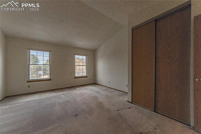 unfurnished bedroom featuring light colored carpet, lofted ceiling, a textured ceiling, and a closet