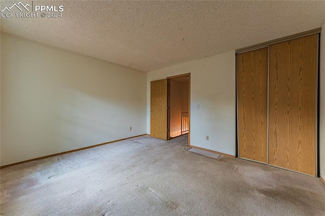 unfurnished bedroom featuring a textured ceiling, light colored carpet, and a closet