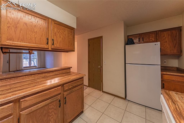 kitchen featuring butcher block counters, light tile patterned floors, and white refrigerator