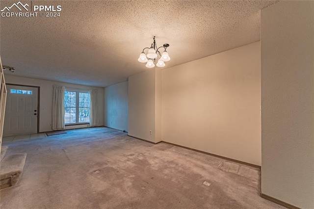 carpeted spare room with a textured ceiling and an inviting chandelier