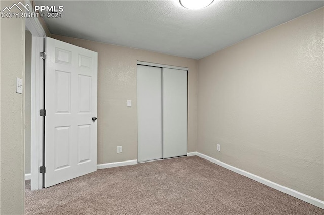 unfurnished bedroom featuring carpet, baseboards, a closet, a textured ceiling, and a textured wall