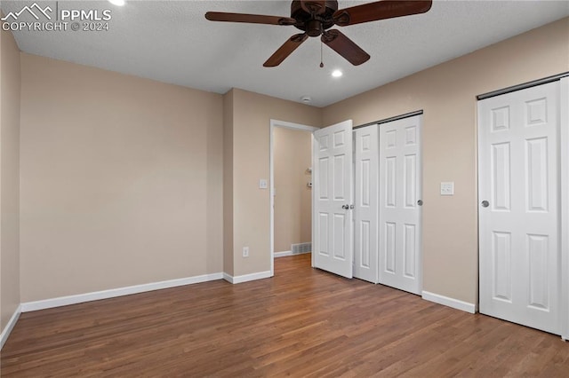 unfurnished bedroom featuring two closets, baseboards, wood finished floors, a textured ceiling, and a ceiling fan