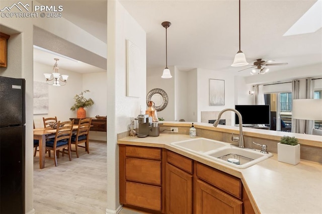 kitchen with pendant lighting, ceiling fan with notable chandelier, black fridge, sink, and light hardwood / wood-style flooring