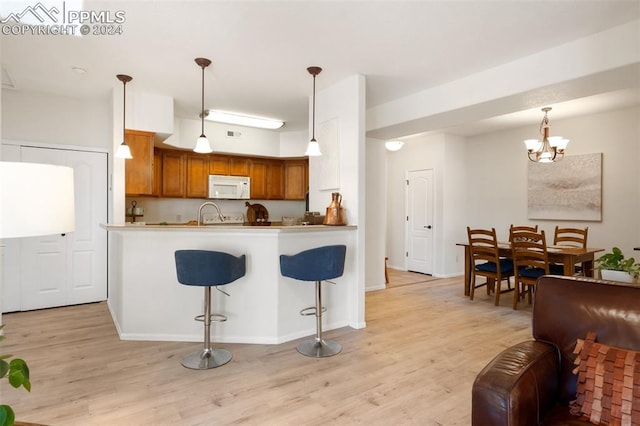 kitchen with a breakfast bar, an inviting chandelier, decorative light fixtures, light hardwood / wood-style floors, and kitchen peninsula