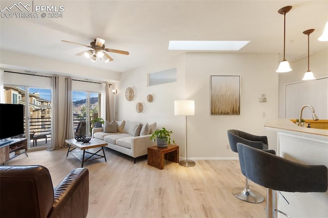 living room with a skylight, light hardwood / wood-style flooring, ceiling fan, and sink