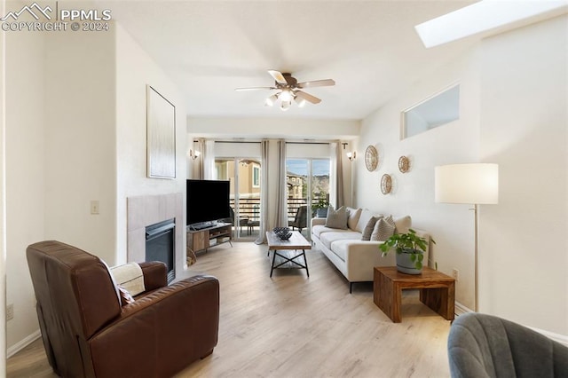 living room featuring ceiling fan, light hardwood / wood-style floors, a fireplace, and a skylight