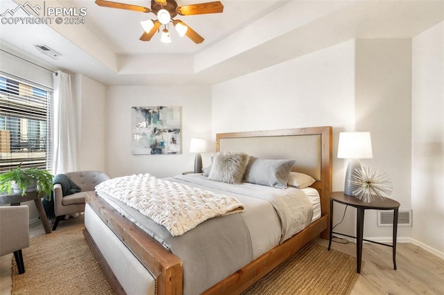 bedroom with a raised ceiling, ceiling fan, and light wood-type flooring