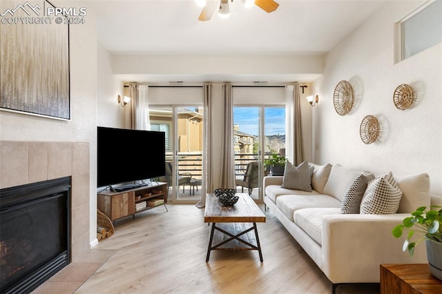 living room with a tile fireplace, light hardwood / wood-style flooring, and ceiling fan