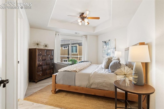 bedroom featuring ceiling fan, light hardwood / wood-style floors, and a raised ceiling