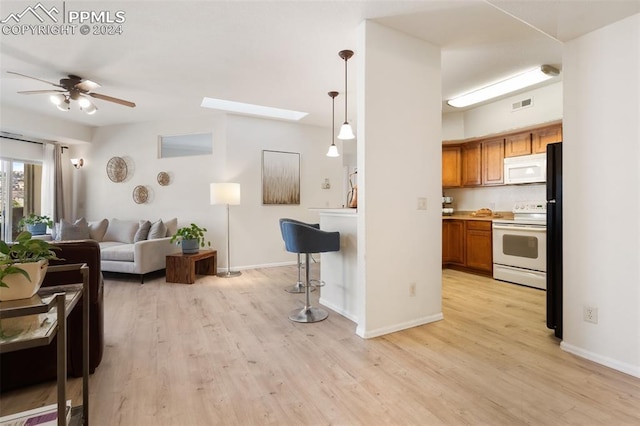 kitchen featuring white appliances, a skylight, ceiling fan, light wood-type flooring, and decorative light fixtures