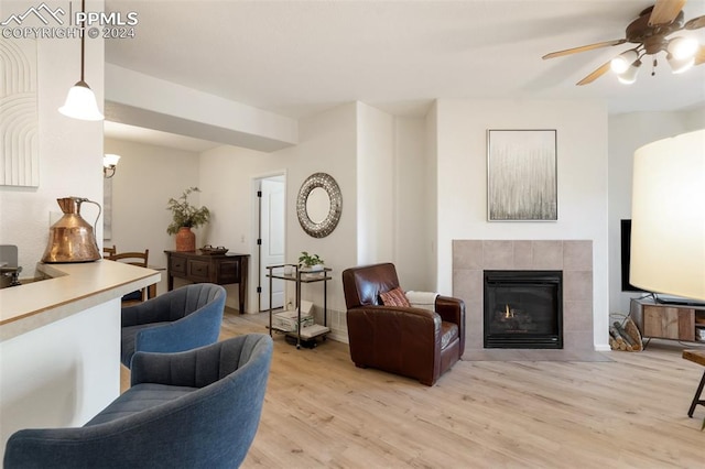 living room with light hardwood / wood-style floors, ceiling fan, and a tiled fireplace