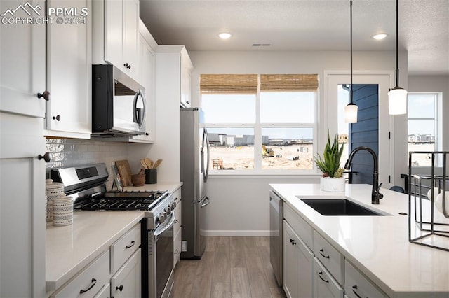 kitchen featuring pendant lighting, backsplash, white cabinets, sink, and stainless steel appliances