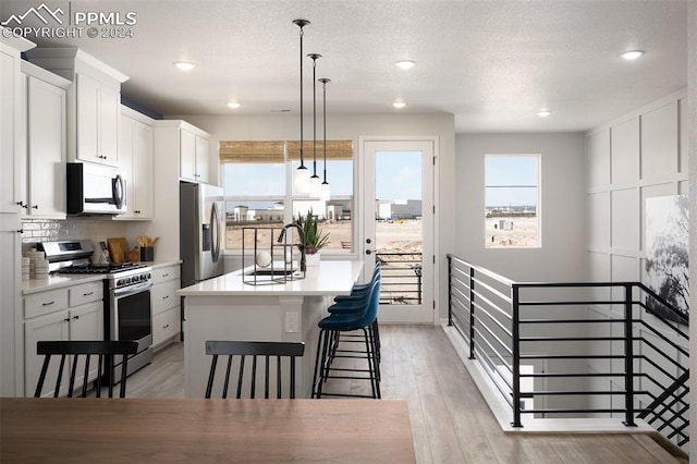 kitchen featuring a kitchen island with sink, white cabinetry, stainless steel appliances, and decorative light fixtures