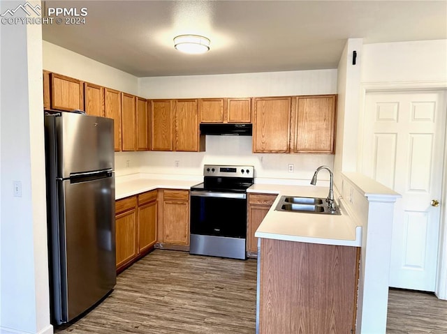 kitchen featuring brown cabinets, stainless steel appliances, light countertops, a sink, and under cabinet range hood