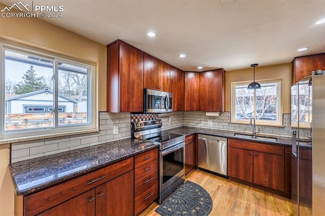 kitchen featuring sink, tasteful backsplash, hanging light fixtures, light hardwood / wood-style flooring, and appliances with stainless steel finishes