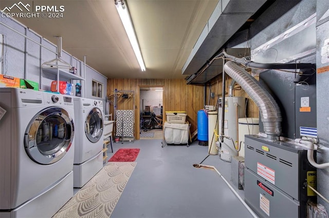 clothes washing area with independent washer and dryer, water heater, and wood walls