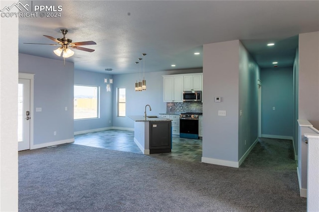 kitchen featuring appliances with stainless steel finishes, tasteful backsplash, a center island with sink, decorative light fixtures, and white cabinetry